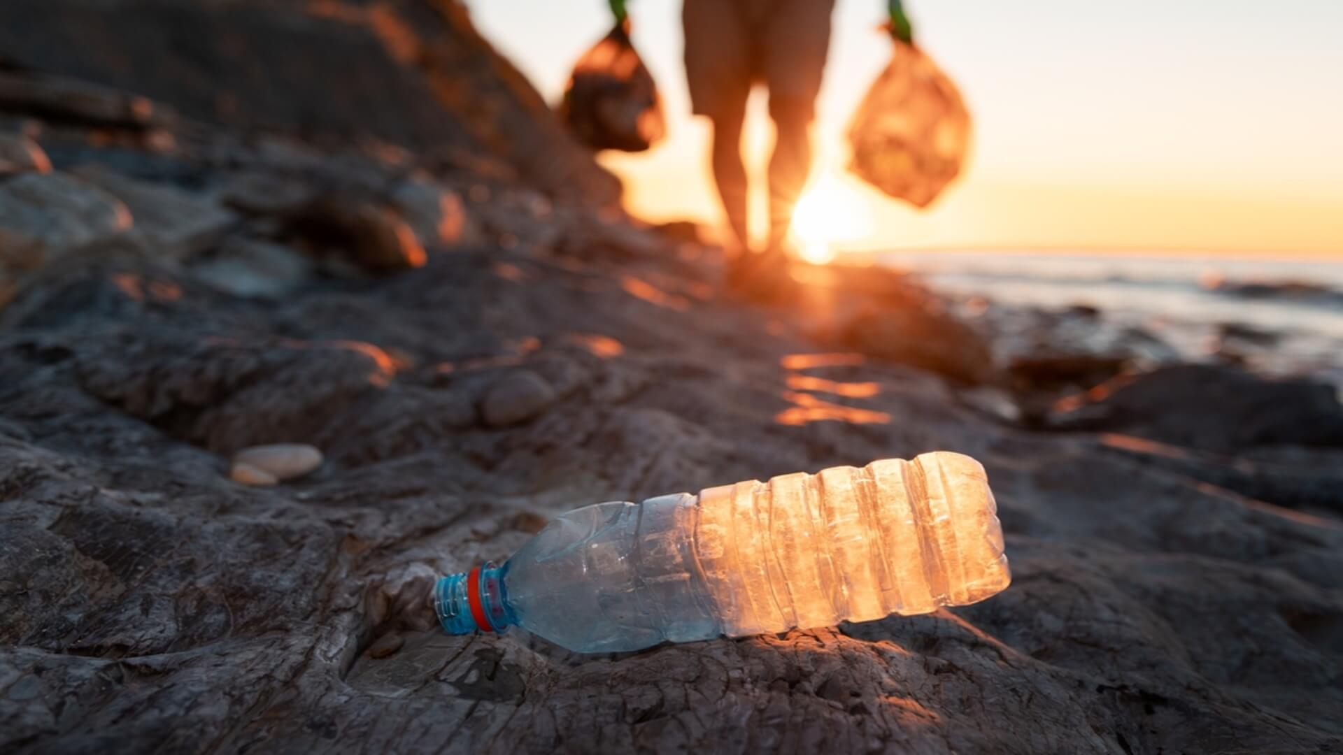 A man collecting trash on the beach goes to pick up a water bottle on a voluntourism opportunity