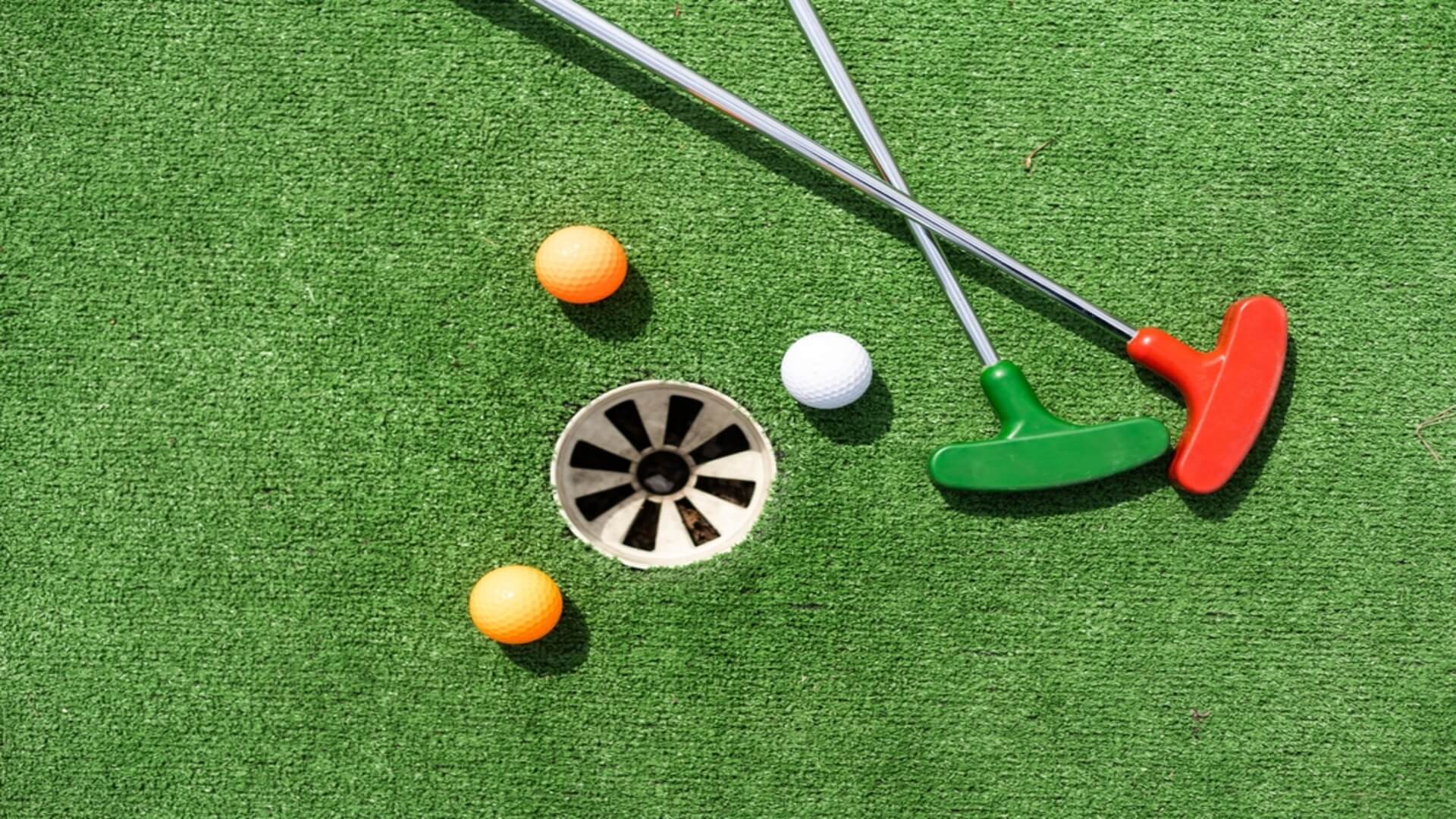 Two putters and three golf balls surround a hole at a Maui mini golf course
